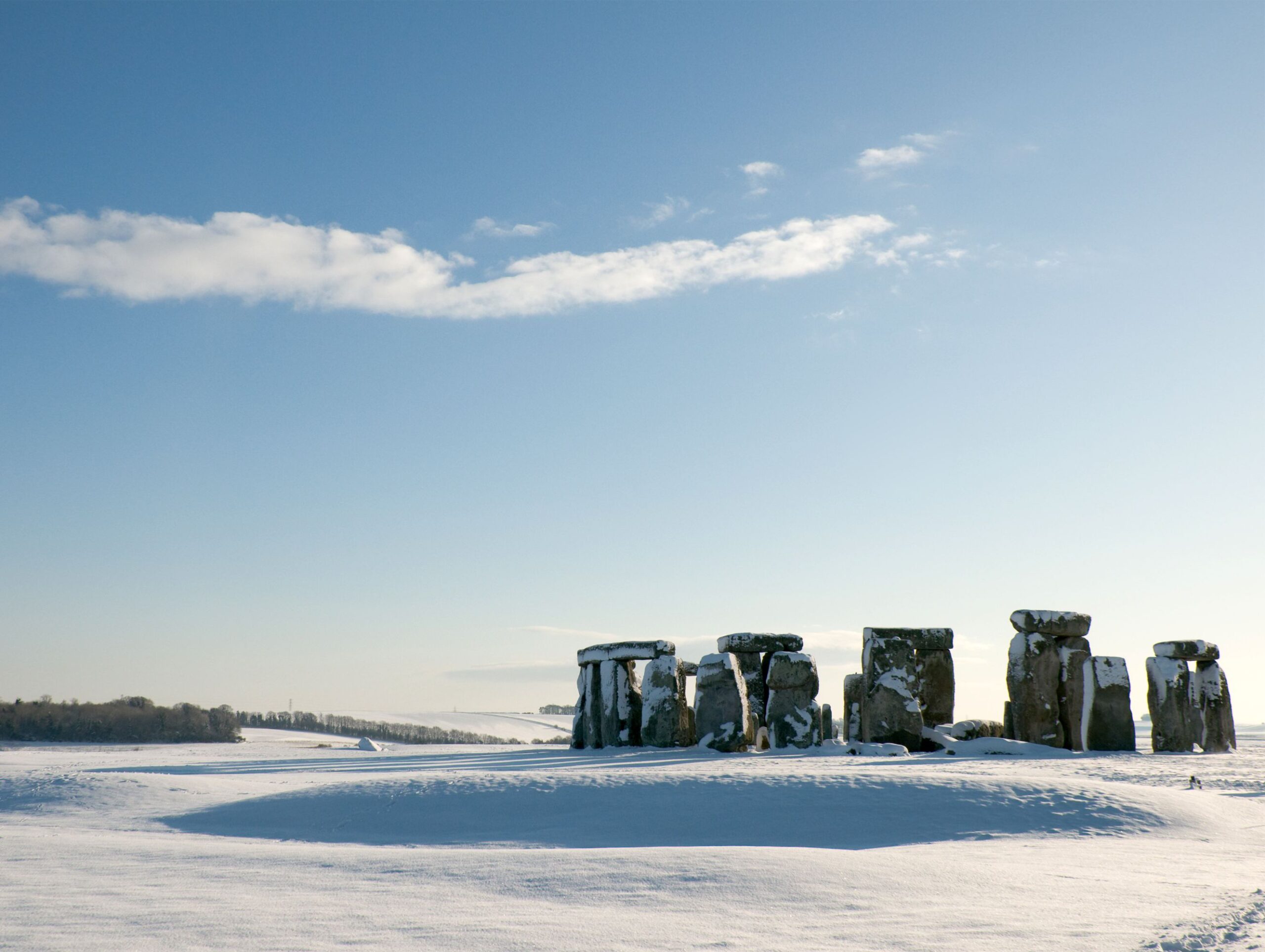 The ancient site of Stonehenge, covered in a blanket of snow on a crisp winter day.