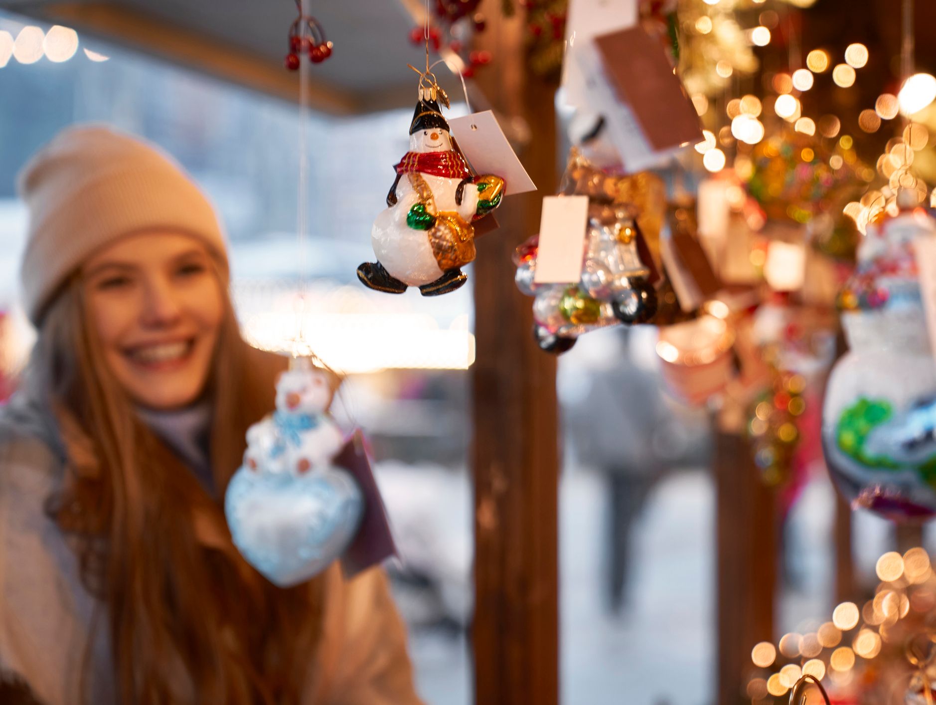A smiling woman admires festive glass ornaments, including snowmen and baubles, at a twinkling Christmas market, capturing the joy of Christmas in Wiltshire.