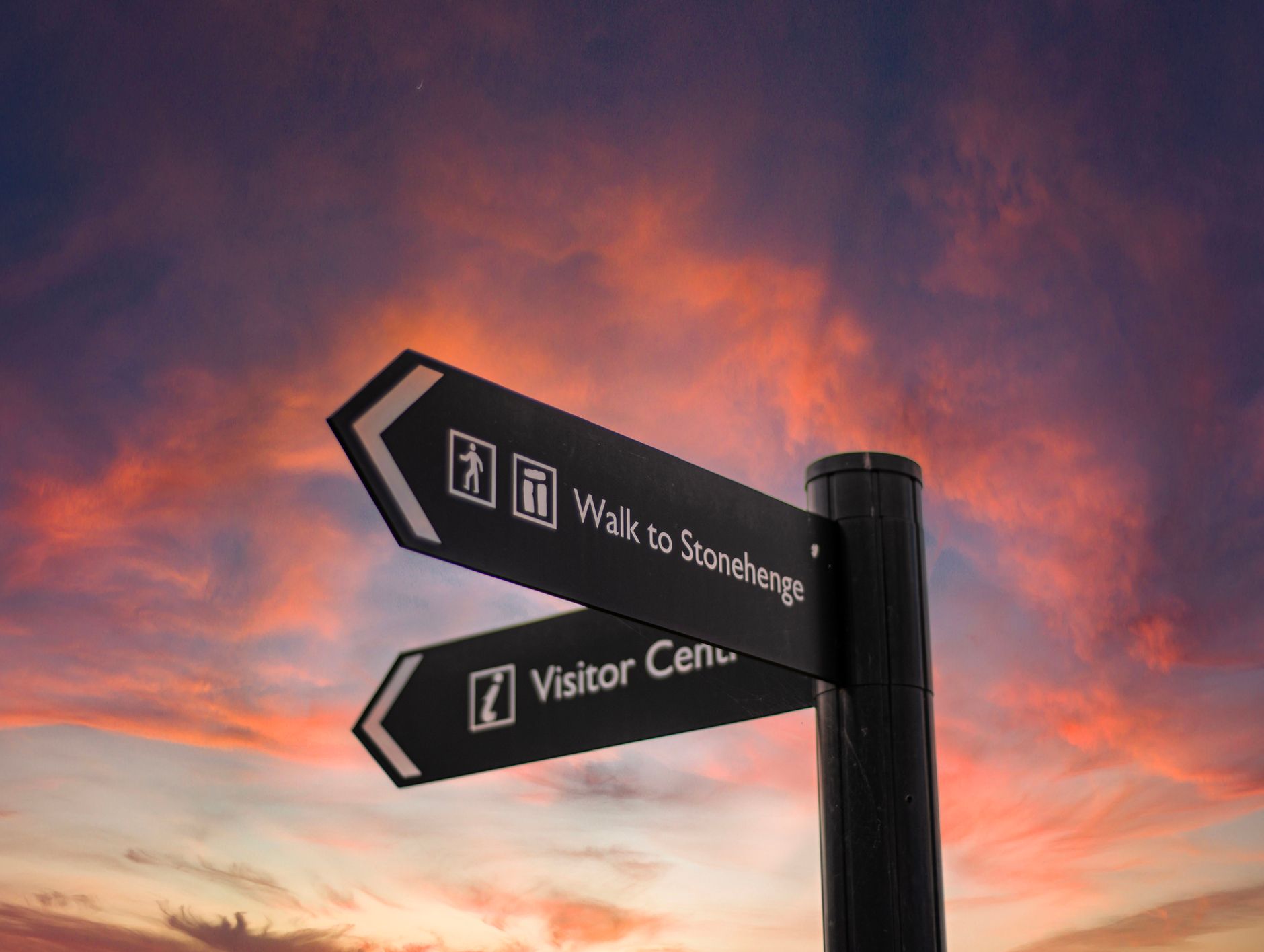 A signpost for a visitor centre and the Stonehenge walk. The sign is in front of a beautiful sunset.