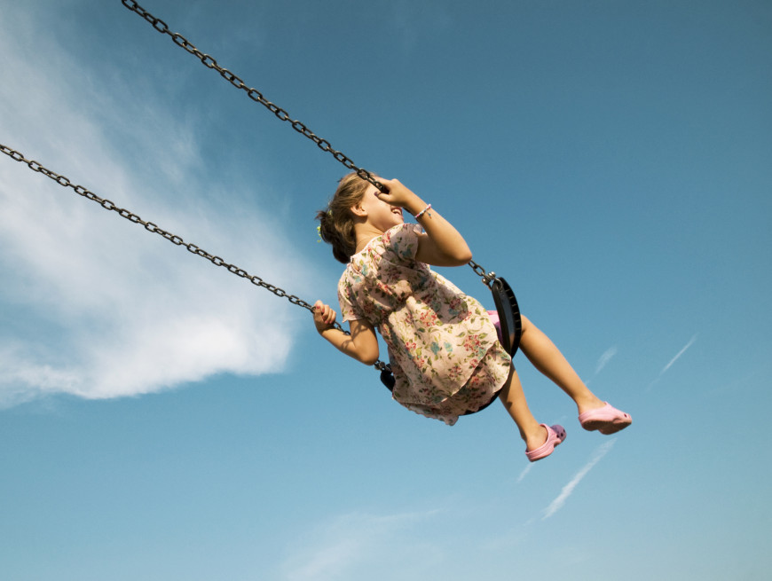 Young girl swinging high, with the sky as a backdrop, wearing a floral dress.
