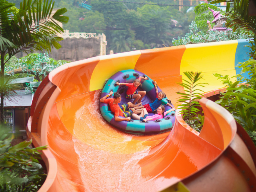 Friends on a circular raft sliding down a vibrant water slide surrounded by greenery.